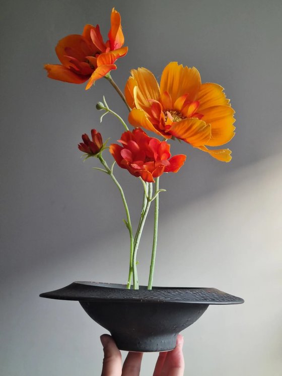 Silk flowers arranged in a black ceramic ikebana bowl, held in hand, from @obsidianandflame
